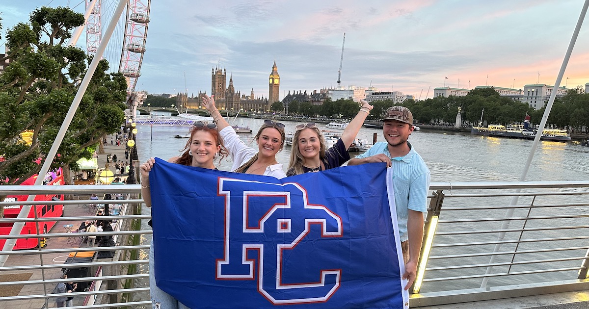 Four PC students with college flag in London. London landmarks in background.