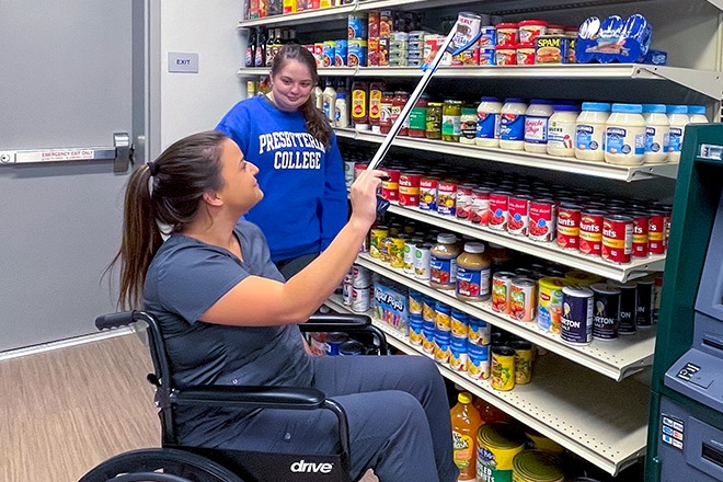 Two students attempting to utilize specialized devices designed for individuals with physical disabilities in order to shop at the grocery store.