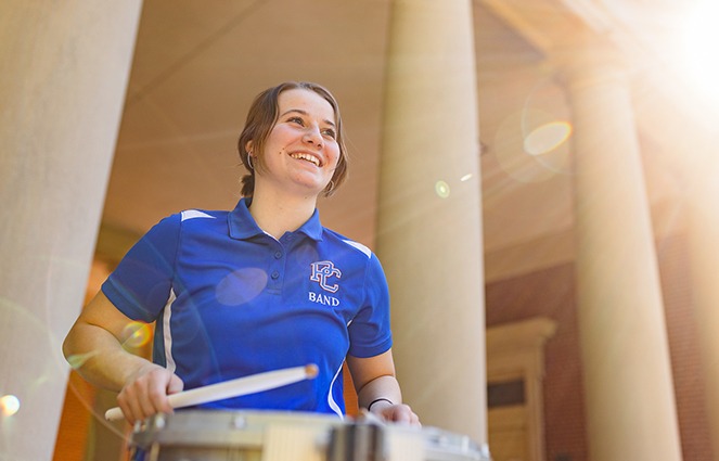 PC Band Student smiling in front of Belk playing drums