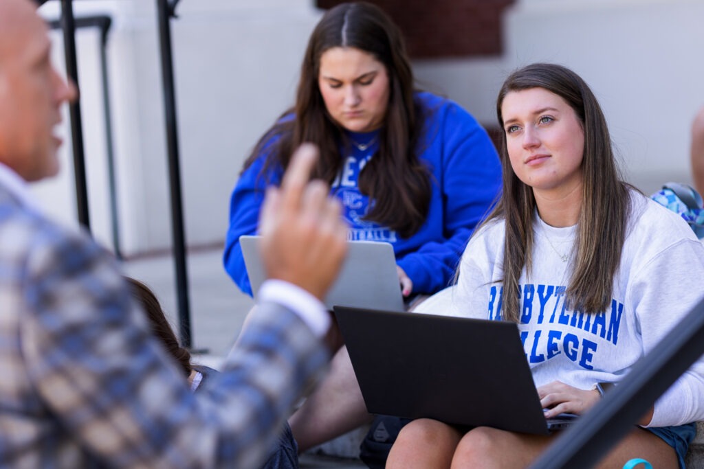 A coed at Presbyterian College listens to her history professor while sitting with a laptop.