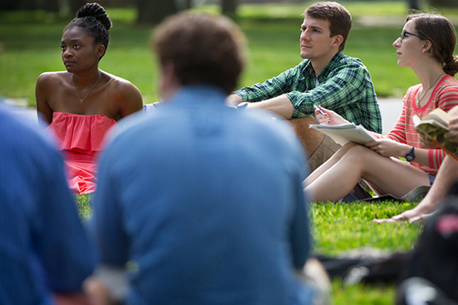 Catholic Association student siting on the grass and taking notes