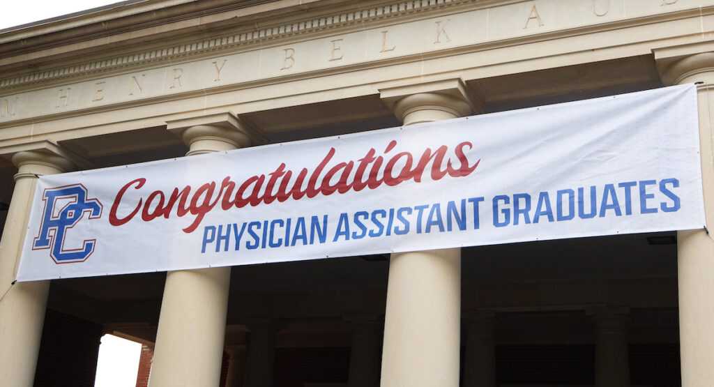 Banner hanging from the loggia at Belk Auditorium reading "Congratulations Physician Assistant Graduates."