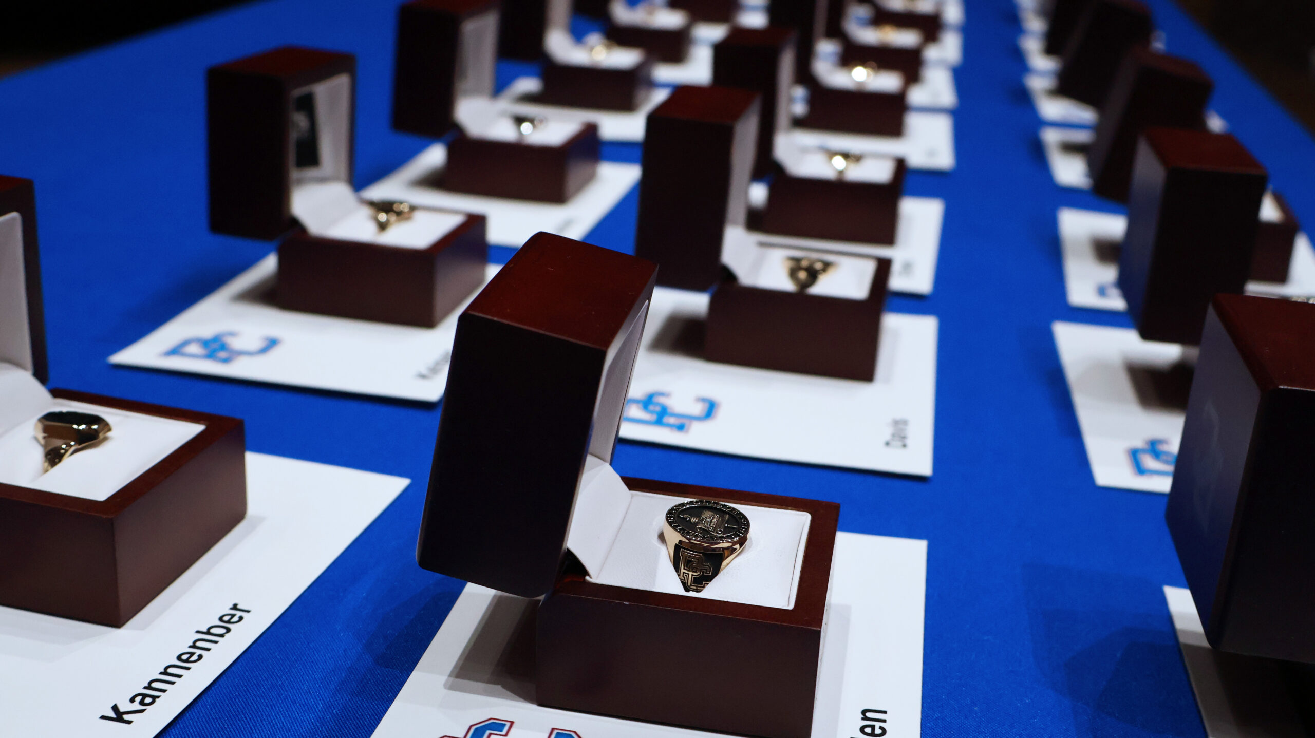 Photo of a table with blue table cloth, and the class rings of 2025 set up in rows with each student's corresponding name tags.