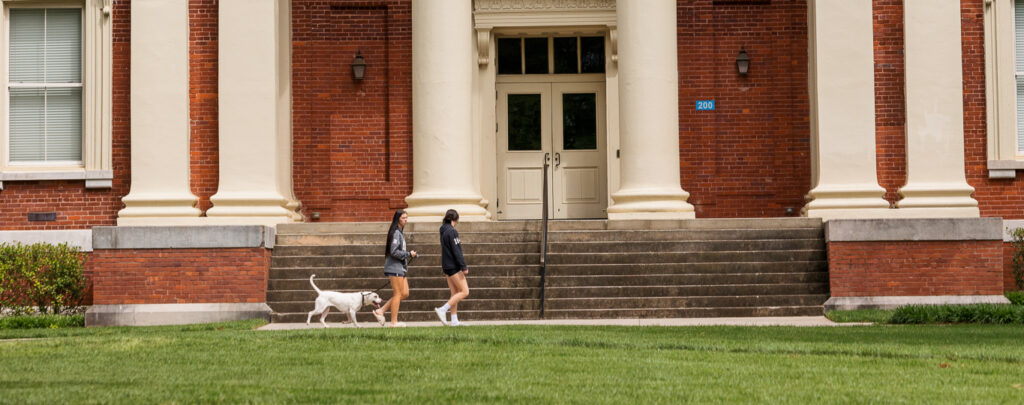 Presbyterian College students walking a dog in front of Neville Hall.