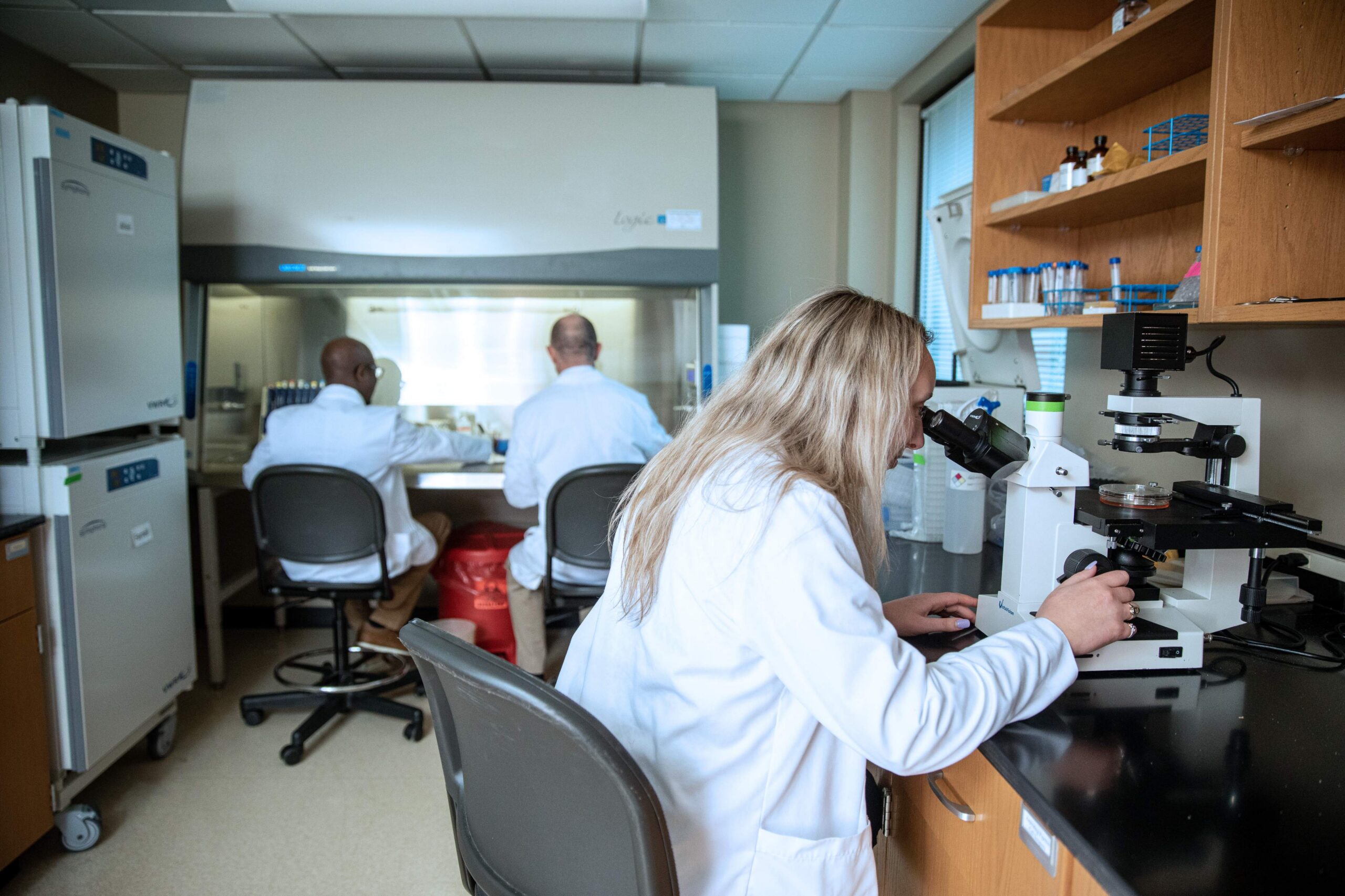 A pharmacy student looks into a microscope in a lab.