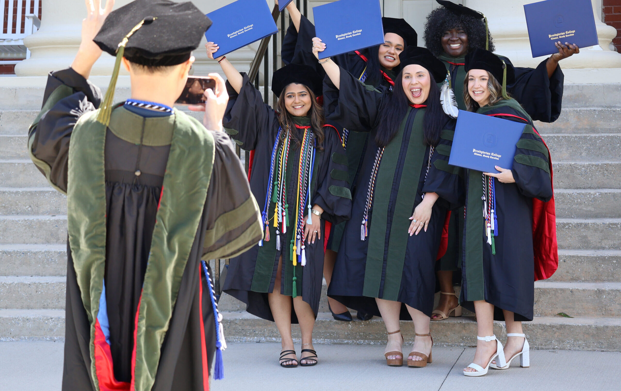 Presbyterian College School of Pharmacy 2026 Hooding and Commencement. Photo of graduate taking a photo of Pharmacy graduates smiling and cheering.