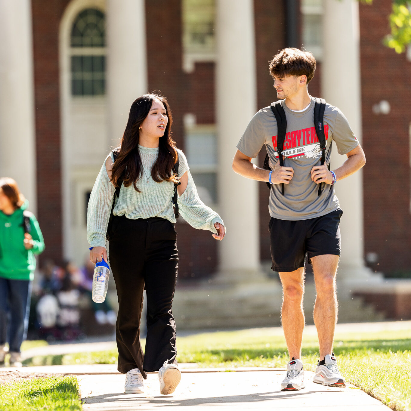 Presbyterian College students walking and talking on a sunny day in front of a historic campus building with white columns.
